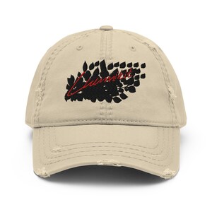 Może przedstawiać: Beżowa, zniszczona czapka z daszkiem z haftowanym wzorem w kolorze czarnym i czerwonym. Wzór przedstawia skupisko liści z napisem "Unburnt" napisanym czerwonym kursywą.