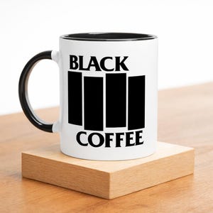 May include: White coffee mug with a black interior and handle. The mug features the words "BLACK COFFEE" in bold black letters with a graphic design of four vertical black bars.