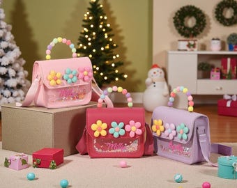 May include: Three colorful purses with flower embellishments and beaded handles. The purses are pink, red, and lavender, with clear front pockets filled with glitter. The purses have matching shoulder straps and are displayed on a neutral surface.