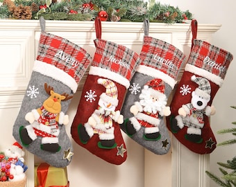 May include: Four Christmas stockings with personalized names: Avery, Jackson, Lucilla, and Daniel. Each stocking features a plaid cuff, a felt body in red or gray, and a festive character: a reindeer, snowman, Santa, and a bear. Snowflakes and stars add to the holiday theme.