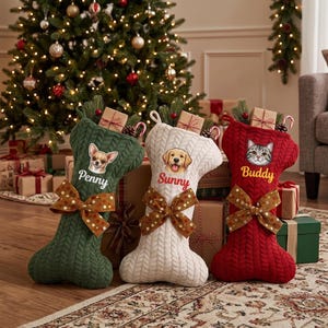 May include: Three bone-shaped Christmas stockings in dark green, white, and red cable knit fabric. Each features a pet portrait, a name embroidered in script, and a brown polka-dot bow. The names Penny, Sunny, and Buddy are visible.