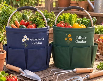 May include: Two cylindrical garden tool bags in navy blue and dark green, each with a metal handle and exterior pockets. The navy bag features a white daisy graphic and the text "Grandma's Garden," while the green bag shows orange flowers and "Selina's Garden."