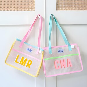 May include: Two mesh tote bags with pastel accents. One bag has yellow trim and the letters "LMR" in yellow. The other bag has green trim and the letters "CNA" in pink. Both bags have pink and blue straps.