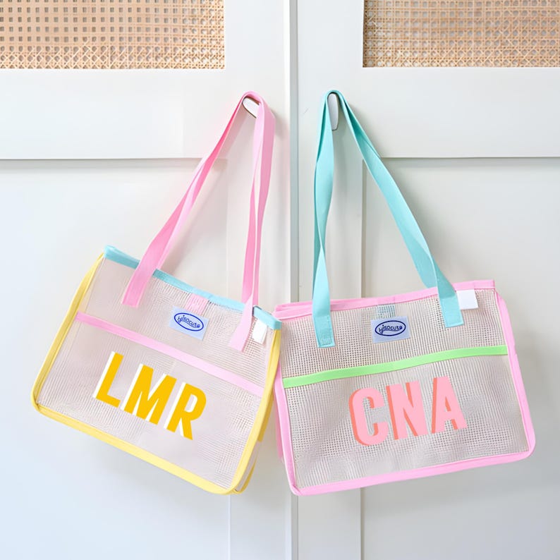 May include: Two mesh tote bags with pastel accents. One bag has yellow trim and the letters "LMR" in yellow. The other bag has green trim and the letters "CNA" in pink. Both bags have pink and blue straps.