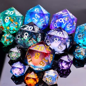 May include: A collection of multi-faceted polyhedral dice in various colors including teal, blue, purple, and red. The dice feature translucent resin, embedded gold flakes, and small floral accents, with white or gold engraved numbers on each face.