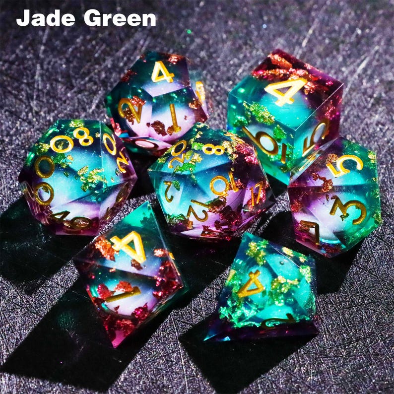 May include: A set of seven polyhedral dice in shades of jade green, teal, and purple. The dice have gold-colored numbers and are filled with gold flakes. The text "Jade Green" is in the upper left corner.