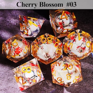 May include: Set of seven polyhedral dice with a cherry blossom design. The dice are clear with gold numbering and red and white floral inclusions. The text "Cherry Blossom #03" is at the top.