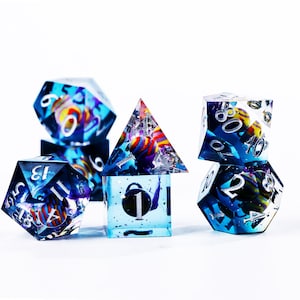 May include: A collection of polyhedral dice in various shapes, including a pyramid, cube, and multi-sided dice. The dice are clear with blue and white accents, and contain colorful, spherical inclusions. Numbers are visible on each die.