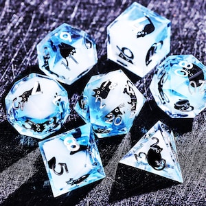 May include: Set of seven polyhedral dice with a blue and white translucent design. Each die features black cat illustrations and silver numbering. The dice are designed for tabletop games.