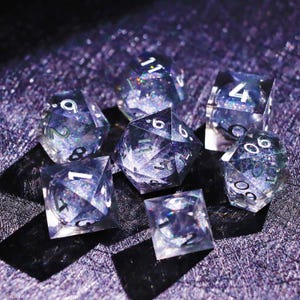 May include: Set of seven clear, multi-sided dice with silver numbering and iridescent glitter suspended within. The dice are arranged on a textured, dark purple surface, casting shadows. Ideal for tabletop gaming.