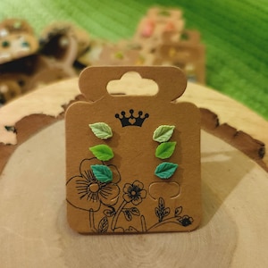 May include: A set of six green leaf stud earrings displayed on a brown card with a crown and heart logo.