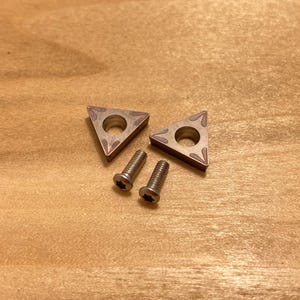 May include: Two silver triangular shaped metal inserts with a hole in the center and a decorative pattern. Two silver screws are also included.