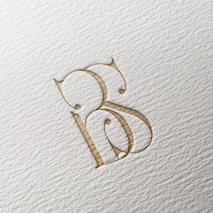 May include: A gold-colored monogram logo featuring the intertwined letters "B" and "S". The design has a classic, elegant style with decorative flourishes and is embossed on a textured white paper.