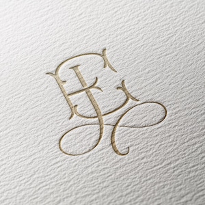 Op de afbeelding: Een goudkleurig monogram met de in elkaar verstrengelde letters E en J, uitgevoerd in een klassiek kalligrafisch schrift met elegante krullen en lussen, in reliëf aangebracht op wit gestructureerd papier met een zichtbare korrel.