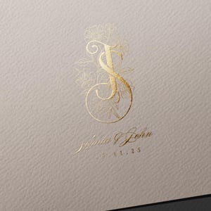 May include: Gold foil monogram featuring the letters "S" and "J" with floral details. The names "Sophia & John" and the date "15.11.25" are printed below the monogram on a textured, light beige background.