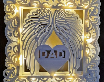Puede incluir: Marco de papel blanco con un corazón que dice "DAD" en su interior. El corazón está rodeado de dos alas de papel blanco. El marco está iluminado con luces LED blancas.