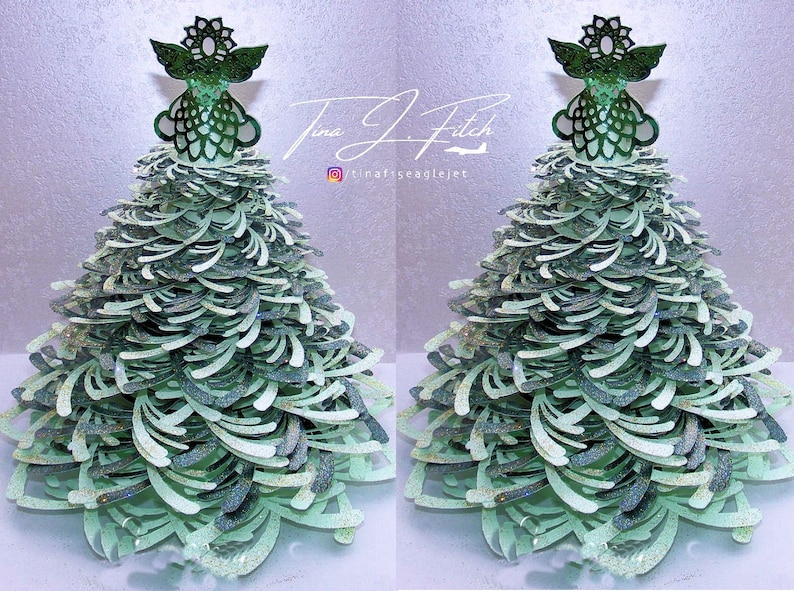 May include: Two green and white paper Christmas trees with a green angel topper. The trees are layered and have a glittery finish. The text "Tina J Fitch" and "@tinafeaglejet" are visible on the image.