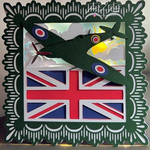 Puede incluir: Un modelo de papel de un avión de combate británico Spitfire volando sobre una bandera de la Union Jack. El modelo está iluminado desde atrás, creando un efecto de sombra.