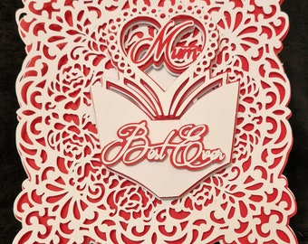 May include: A white card with a red lacy border. The card is folded in half and has a white insert with the words "Mum" and "Best Ever" in a cursive font. The card is decorated with a red heart.