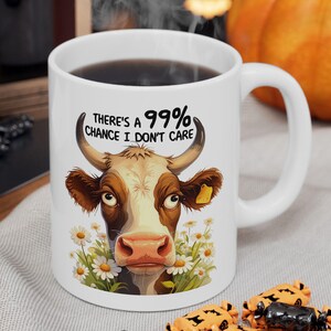 May include: White ceramic coffee mug with a black handle. The mug has a cartoon cow with the text "There's a 99% chance I don't care" printed on it.