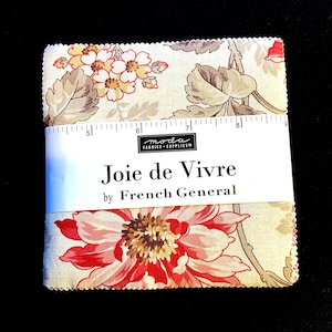 May include: Fabric squares with a floral design in red, cream, and brown. The fabric is wrapped with a white label that reads "Joie de Vivre by French General". A ruler is placed on top of the fabric.
