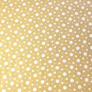 May include: A close-up of fabric featuring a repeating pattern of white polka dots on a golden yellow background. The dots are of varying sizes and are evenly spaced.