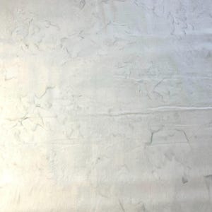 May include: A textured, off-white fabric with subtle variations in tone and pattern. The surface appears to have a slightly marbled effect, with soft, flowing lines and a gentle, organic feel. The fabric is likely a natural fiber.
