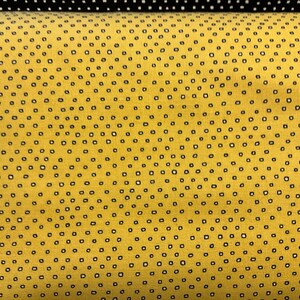 May include: Close-up of a yellow fabric with a repeating pattern of small, black, square-shaped dots. The fabric has a textured appearance. A section of black fabric with white dots is visible at the top.