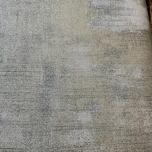 以下が含まれることがあります： 抽象的で風化したデザインのテクスチャード加工された生地。カラーパレットには、グレー、ベージュ、白の色合いが含まれており、ブラシストロークのようなパターンが見えます。生地は微妙で斑点のある外観をしています。