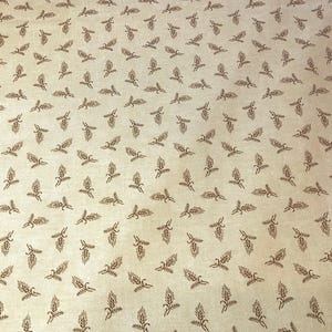 May include: Tan fabric with a repeating pattern of brown wheat stalks. The wheat stalks are evenly spaced across the fabric, creating a consistent and detailed design. The fabric has a slightly textured appearance.