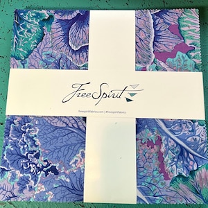 May include: A stack of fabric squares with a floral pattern in shades of blue, purple, and teal. The fabric is wrapped with a white band that has the words "Free Spirit" in script and the website address freespiritfabrics.com.