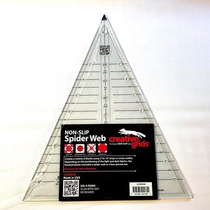 May include: A clear, triangular non-slip Spider Web quilting ruler with measurements in inches. The ruler has a black label with the text "NON-SLIP Spider Web creative grids" and instructions. The ruler is designed for creating spider web or four-piece star blocks.