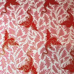 May include: A repeating pattern featuring red dragons with gold accents and pink foliage on a white background. The dragons have outstretched wings and are interspersed among the leaves. The design is suitable for fabric or wallpaper.
