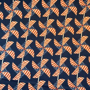 May include: A repeating pattern of red, white, and blue pinwheels against a dark blue background. The pinwheels feature red and white stripes and blue sections with white stars, creating a patriotic design.