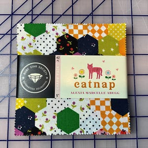 Peut inclure: Un ensemble de carrés de tissu avec divers motifs, dont des pois, des imprimés floraux et des formes géométriques. Le tissu est maintenu par une étiquette indiquant "catnap" et "Ruby Star Society". Le paquet de charme mesure 12.7 cm.