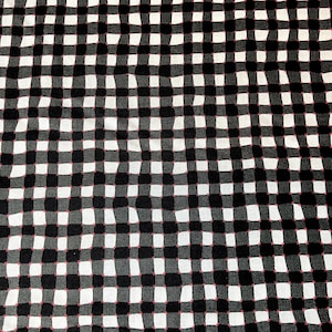 Może przedstawiać: Czarno-biała tkanina w kratę z wzorem gingham. Kwadraty są lekko nieregularne, co nadaje tkaninie ręcznie robiony wygląd. Wzór to klasyczny design, odpowiedni do różnych projektów rzemieślniczych.