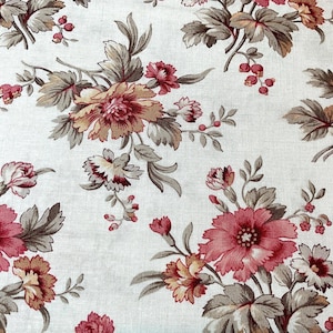 Op de afbeelding: Close-up van een bloemenstof met een herhalend patroon van grote, bloeiende bloemen. De bloemen zijn voornamelijk in tinten rood, roze en perzik, met groene en bruine bladeren. De achtergrond is lichtcrème van kleur.