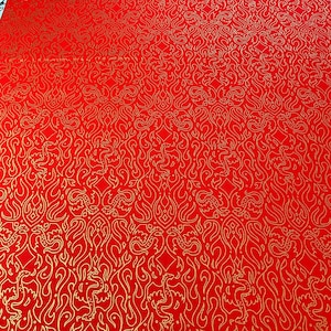 May include: Red fabric with a repeating gold pattern of stylized flames and mythical creatures. The design is symmetrical, with the gold elements contrasting against the vibrant red background. The fabric has a smooth texture.