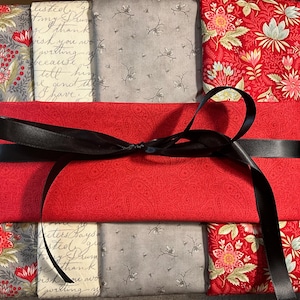 Puede incluir: Un regalo envuelto en tela de cachemira roja, atado con una cinta de satén negro. El regalo está rodeado de telas estampadas en diseños florales rojos, florales grises y grises con escritura. El texto en la tela dice "listed my I thank wish you writing because tell him and I have."