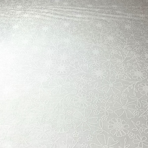 May include: White fabric with an embossed floral pattern. The design features various sizes of flowers and leaves, creating a textured surface. The fabric has a subtle sheen, adding depth to the design. Ideal for crafting or home decor projects.