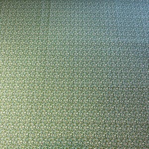 Pode incluir: Close-up de um tecido com um padrão repetido de pequenas flores brancas e azul claro sobre um fundo verde. O tecido tem uma aparência texturizada e um gradiente sutil de verde a azul.