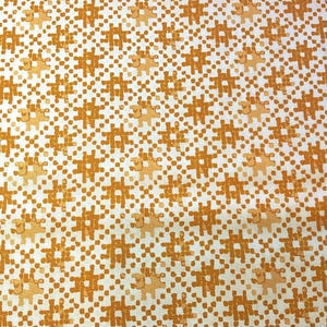 May include: Close-up of a fabric with a repeating pattern of orange and white shapes. The design features a grid-like arrangement of orange puzzle piece shapes and dots on a white background. The fabric has a textured appearance.