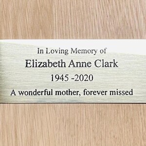 Può includere: Una targa commemorativa rettangolare in metallo color oro spazzolato con quattro fori per viti agli angoli. Il testo nero inciso recita: In Loving Memory of Elizabeth Anne Clark, 1945-2020, A wonderful mother, forever missed. La targa ha una finitura liscia.