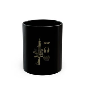 May include: Black ceramic mug with a graphic of a rifle, sunglasses, headphones, and gloves. The graphic is in a light brown color.