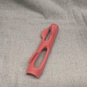 Pu&ograve; includere: Un oggetto allungato color corallo con un design curvo e aperto. L'oggetto presenta due grandi aperture ovali e diversi ritagli curvi pi&ugrave; piccoli. La parte superiore ha una forma arrotondata con due piccoli elementi sporgenti. Il fondo &egrave; aperto e curvo.