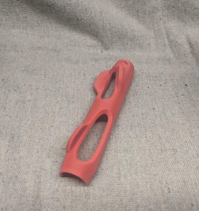 Pu&ograve; includere: Un oggetto allungato color corallo con un design curvo e aperto. L'oggetto presenta due grandi aperture ovali e diversi ritagli curvi pi&ugrave; piccoli. La parte superiore ha una forma arrotondata con due piccoli elementi sporgenti. Il fondo &egrave; aperto e curvo.