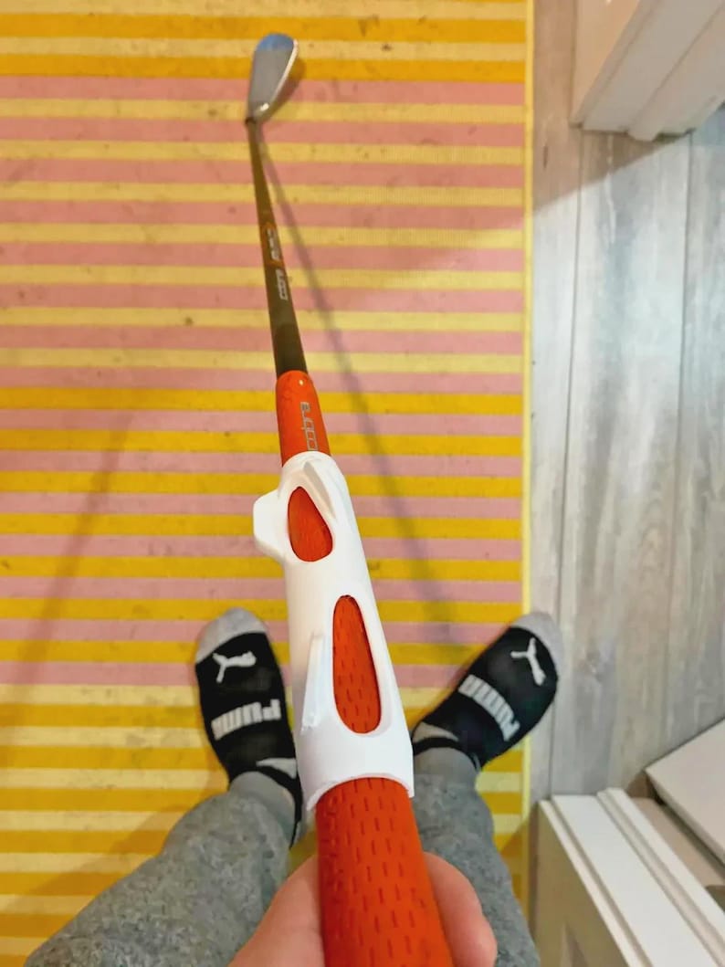 Pu&ograve; includere: Una mazza da golf con una testa argentata e un'asta marrone. L'impugnatura &egrave; arancione con un ausilio per l'allenamento bianco. L'immagine &egrave; ripresa in prima persona.