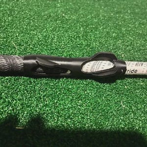 Pu&ograve; includere: Un'impugnatura per mazza da golf nera con una superficie strutturata e un ausilio per l'allenamento nero. L'impugnatura &egrave; su una superficie verde. La parola "ride" &egrave; visibile sulla mazza.
