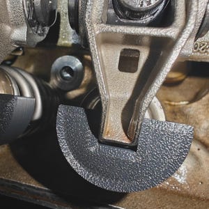 May include: Close-up of engine components, showcasing a rocker arm and a textured, semi-circular piece. The metal parts are in shades of gray and silver, with a focus on mechanical details and textures.