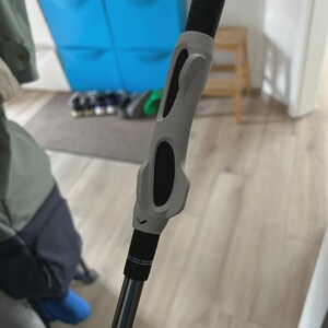 Pu&ograve; includere: Una mazza da golf con un'impugnatura nera e un'attrezzatura di allenamento grigia attaccata. L'attrezzatura di allenamento ha dettagli neri ed &egrave; progettata per aiutare con l'impugnatura e la meccanica dello swing. La mazza &egrave; argento e nera.